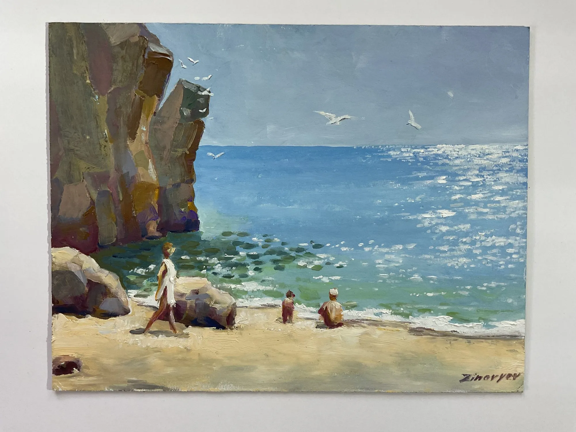 Painting “Studies: By the Ocean, Near the Rocks” by Oleksandr Zinovyev: A sunny beach under a tall rock cliff, people resting on the sand by a sparkling sea.