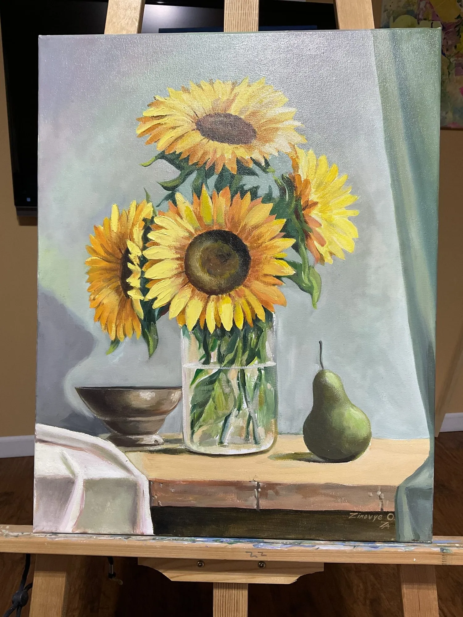 Painting “Still Life with Sunflowers” by Oleksandr Zinovyev: Sunflowers in a glass jar with a green pear and a small bowl; photographed on the easel.