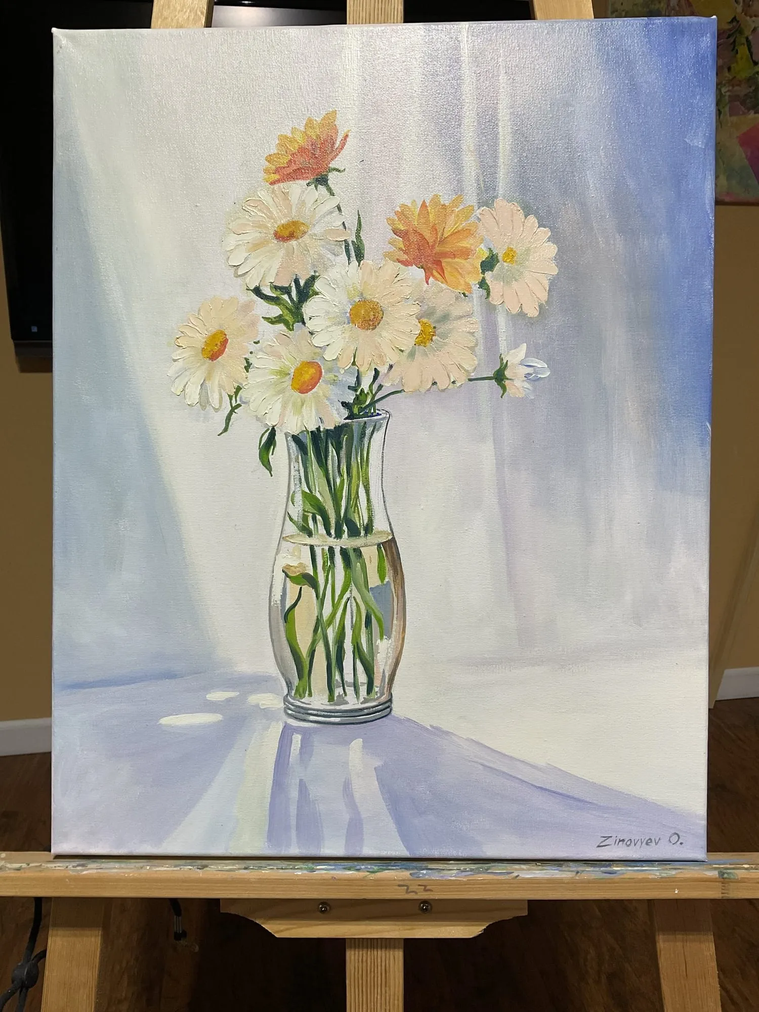 Painting “Daisies” by Oleksandr Zinovyev: White and orange daisies in a glass vase on white cloth; photographed on the easel.